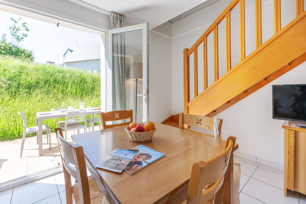 A dining area with a wooden table, chairs, a basket of fruit, and a magazine.