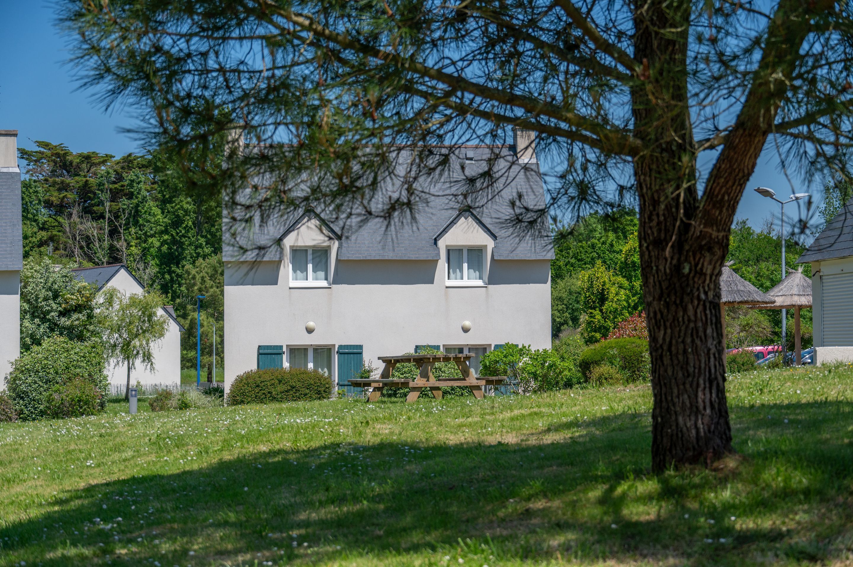A two-story house with a picnic table in the front yard, surrounded by greenery and trees.