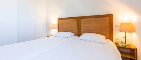 A neatly made bed with white linens in a hotel room. There are two bedside tables with lamps, one on each side of the bed.