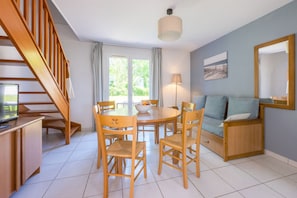 A dining area with a table, chairs, a sofa, a TV, and a staircase. - Résidence Odalys Horizon - Presqu'Ile de Crozon (Crozon)