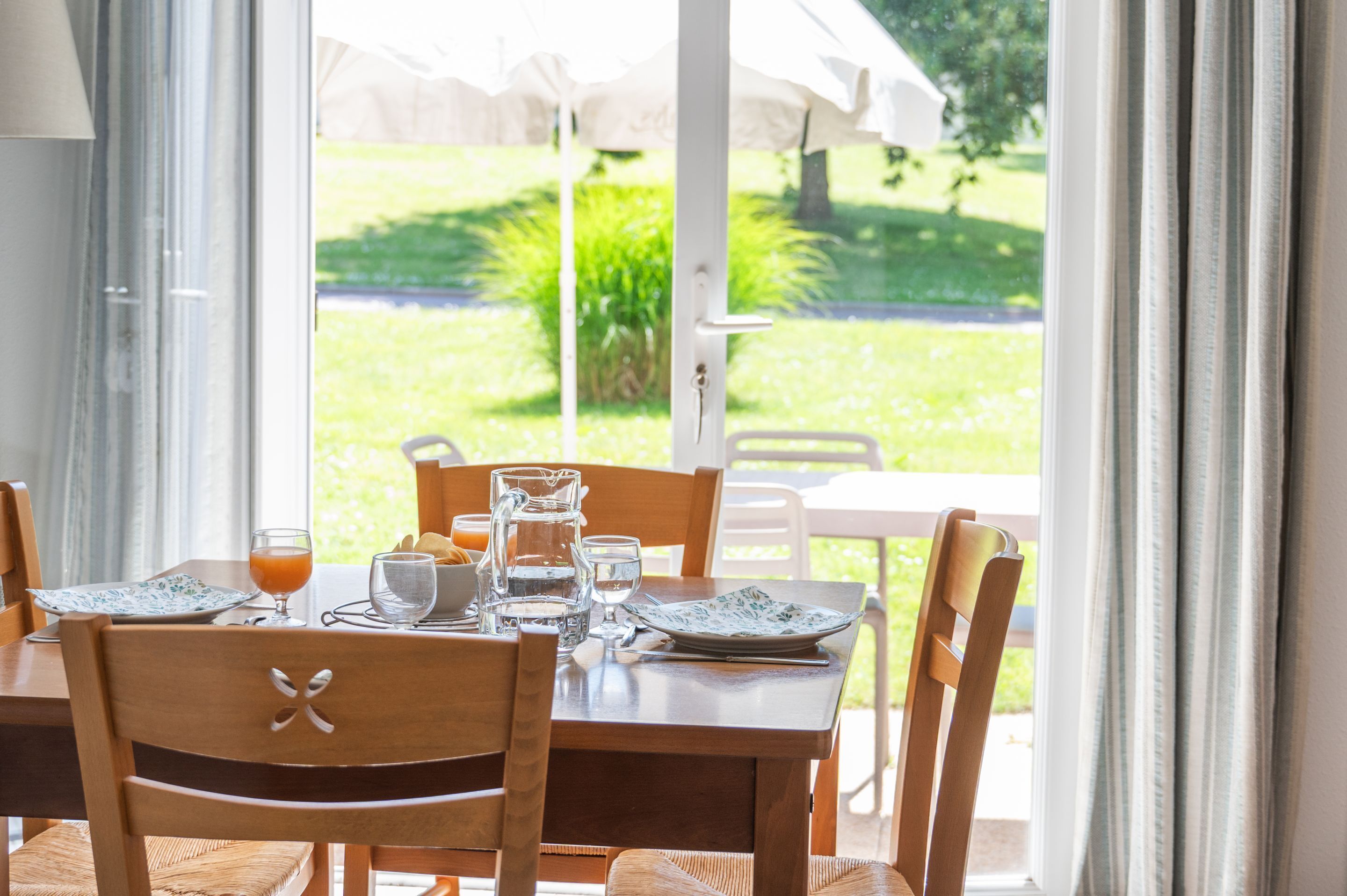 Une table à manger dressée avec des assiettes, des verres et un pichet, entourée de chaises.