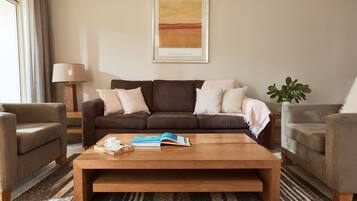 A living room with a brown sofa, two armchairs, a wooden coffee table, and a framed abstract painting on the wall.