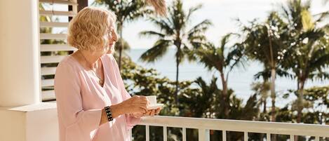 Eine Person steht auf einem Balkon mit Blick auf Palmen und das Meer.