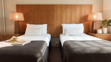 A hotel room with two beds, wooden headboard, bedside lamps, a small potted plant, and a book on the left bed.