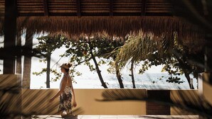 A person walking in a covered outdoor area with a view of the ocean and trees. - Sea Change Beachfront Apartments (Trinity Beach)