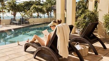 Zona junto a la piscina con sillones de descanso, piscina y plantas en macetas.