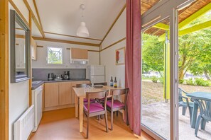 A compact kitchen with wooden cabinets, a dining table with chairs, and a view of a garden through a glass door.