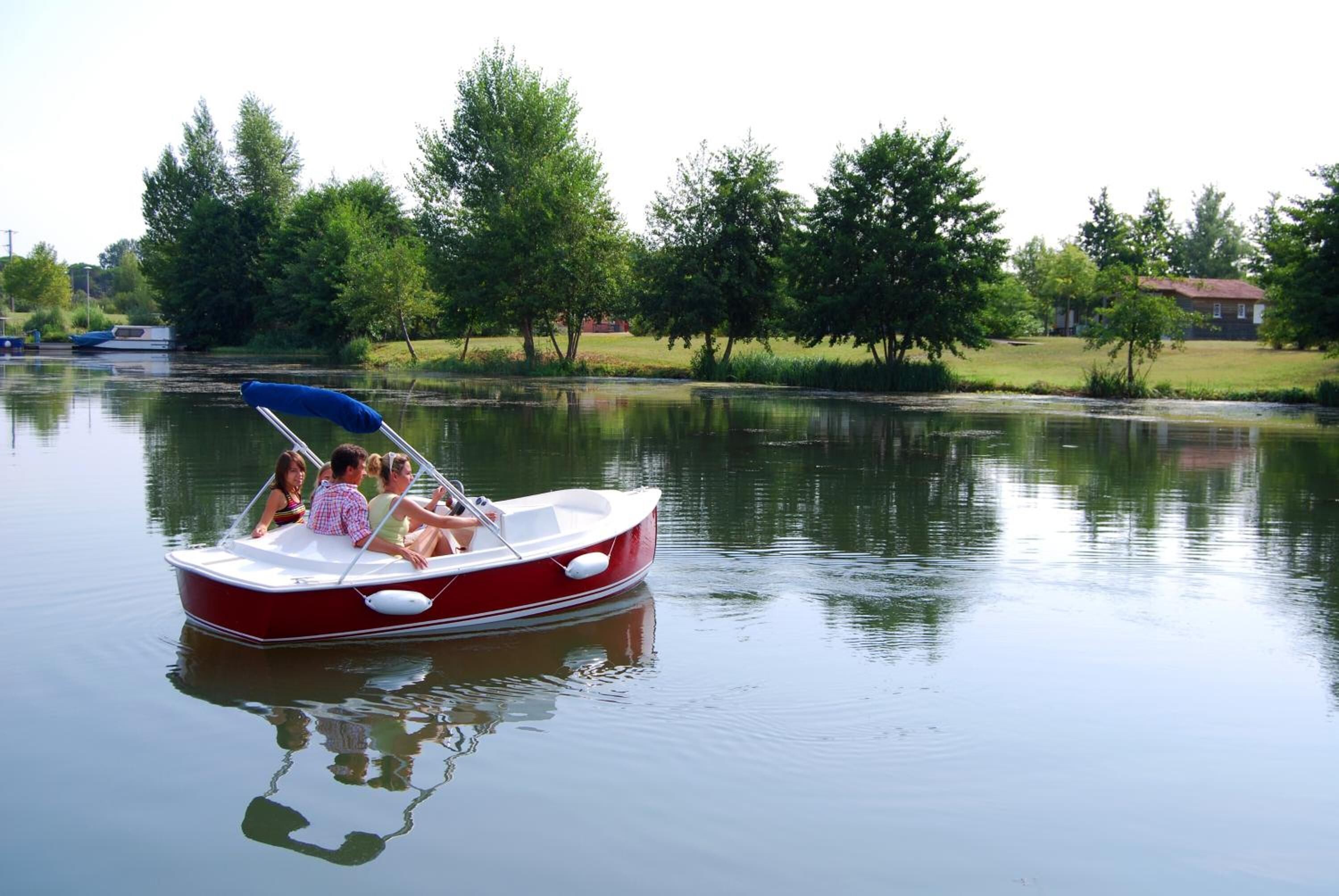 A small red and white boat with a blue canopy on calm water.