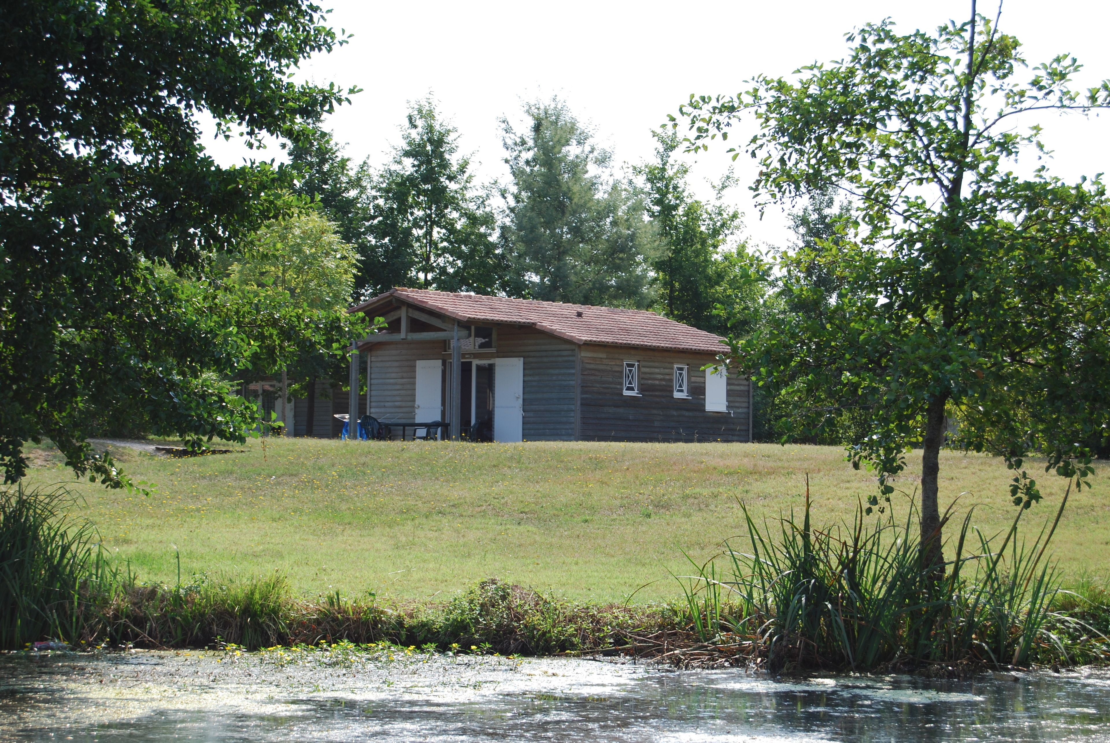 A wooden cabin with a red roof, situated on a grassy field with trees in the background.