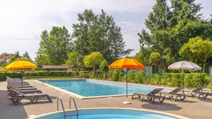 A swimming pool with lounge chairs and umbrellas, surrounded by trees and a clear sky.