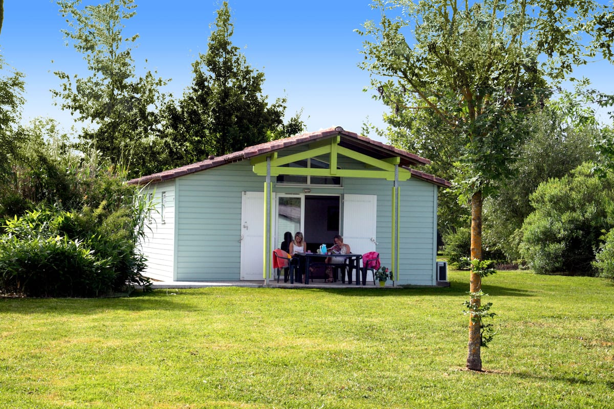 A small, single-story building with a porch, surrounded by greenery.