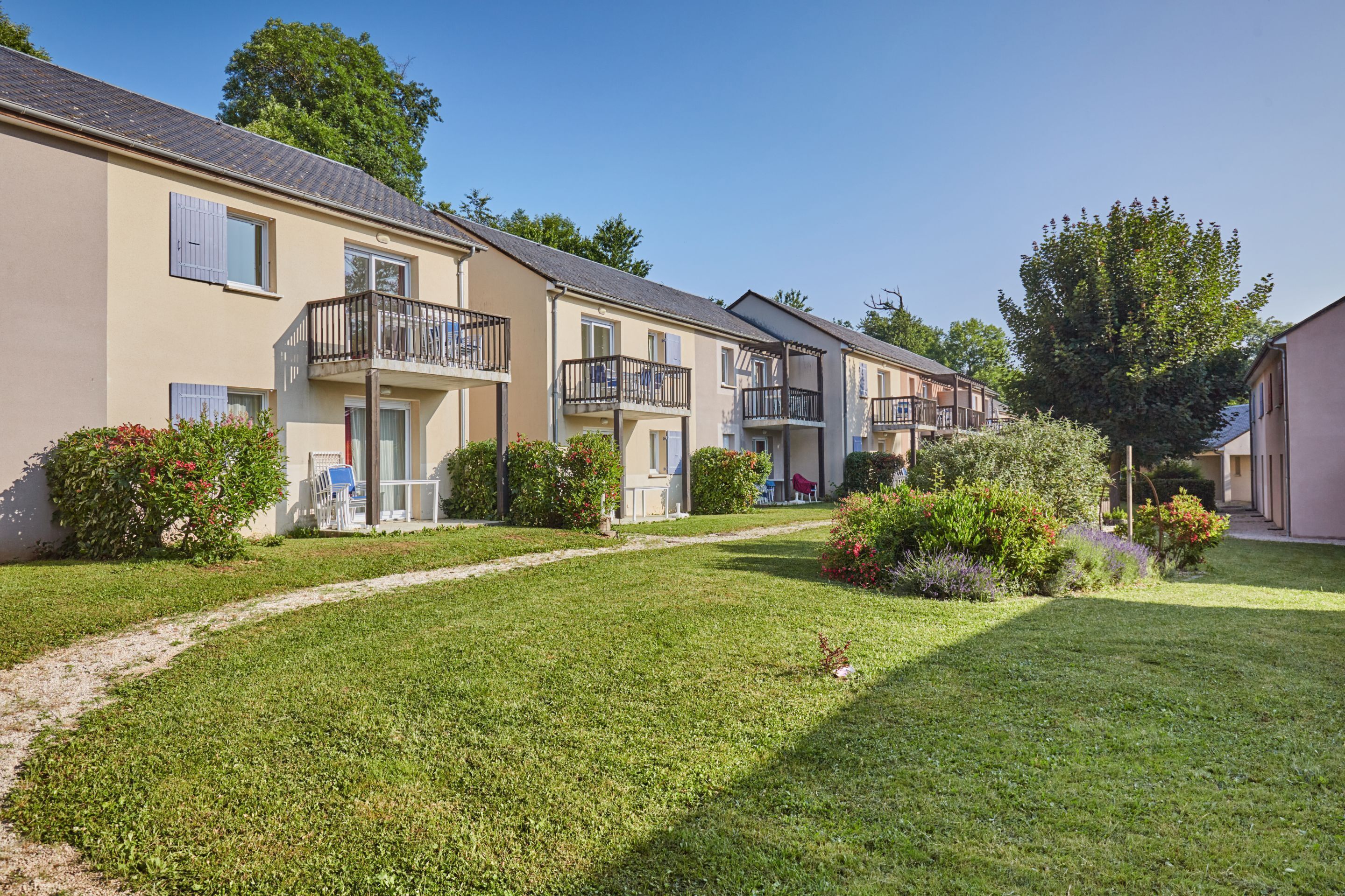 A row of townhouses with balconies, a well-maintained lawn, and a clear sky.