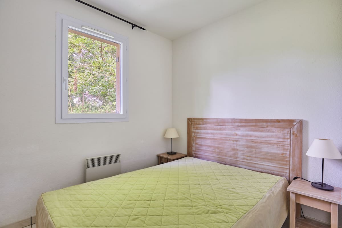 A bedroom with a bed, a window, a nightstand, and a lamp.