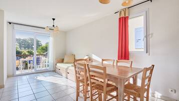 Un coin repas avec une table et des chaises en bois, une porte-fenêtre coulissante donnant sur un espace extérieur aménagé, et un rideau rouge à la fenêtre.