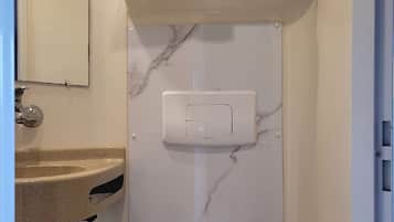 A bathroom with a marble wall, a toilet, a sink, and a towel rack.
