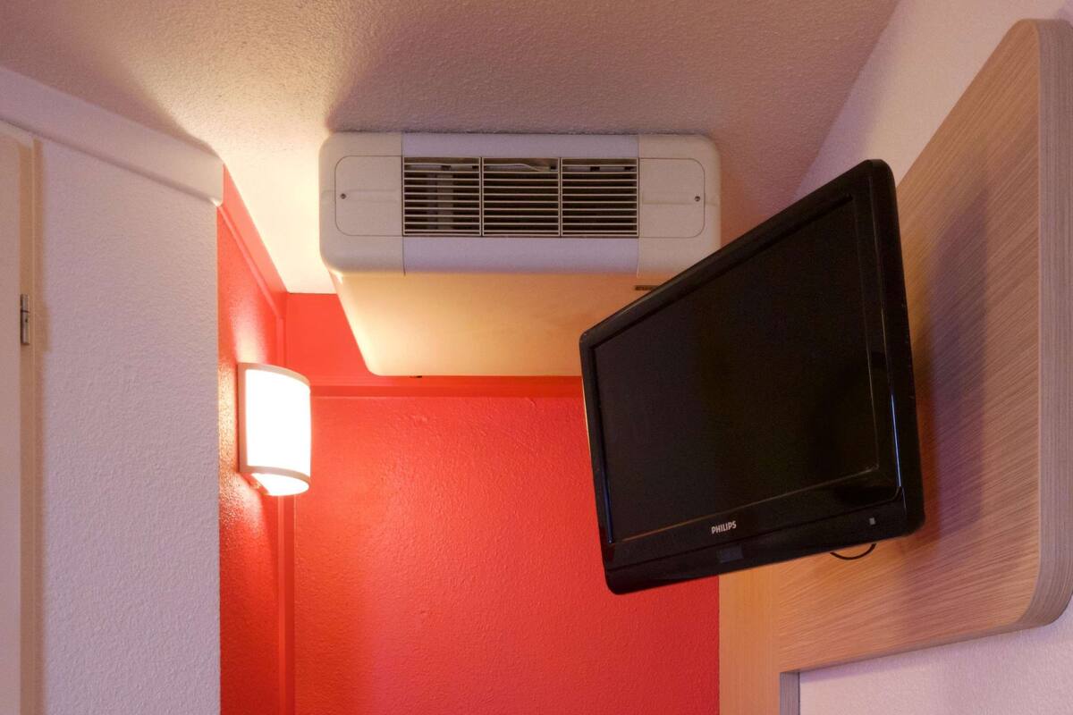 A compact room with a red wall, a mounted television, a small table, and a chair.