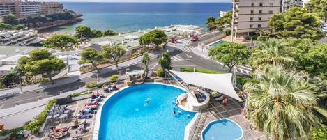 A swimming pool with a view of the sea, surrounded by lounge chairs and umbrellas.