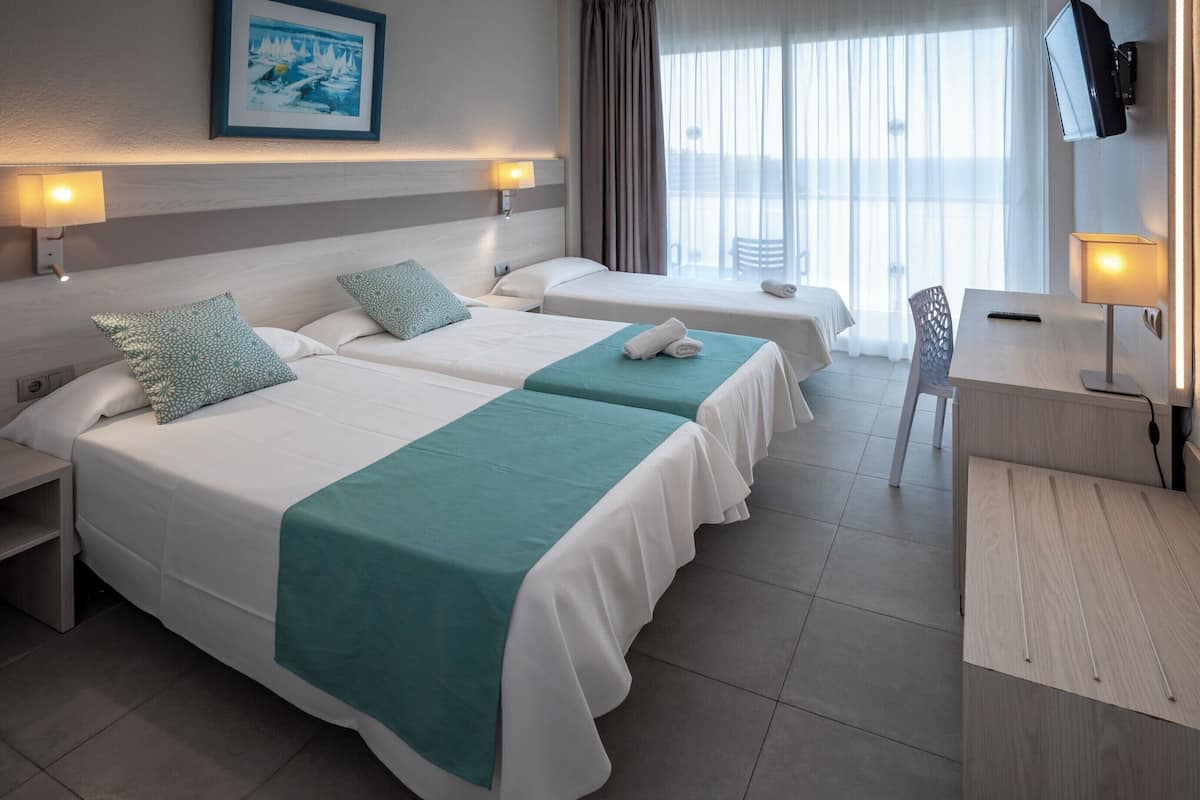 Quarto de hotel com duas camas, uma escrivaninha, uma televisão e janela com cortinas.
