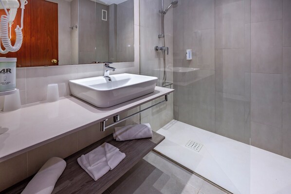 A modern bathroom with a large sink, a glass shower enclosure, and a wooden door. - 4R Salou Park Resort I (Salou)