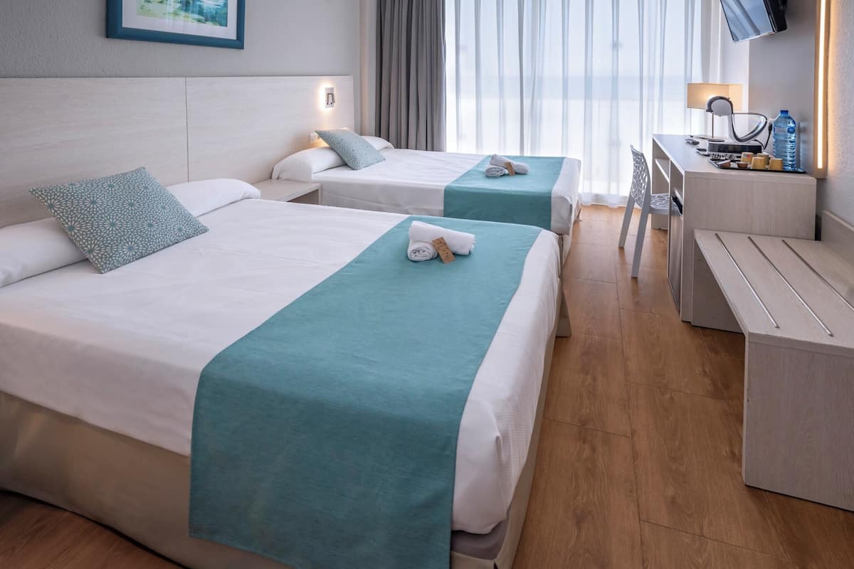 Quarto de hotel com duas camas, uma mesa e uma televisão.