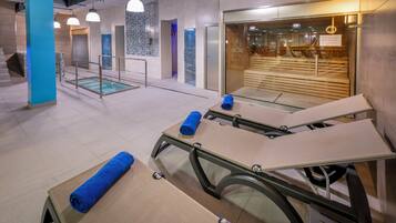 Un área de spa moderna con camillas de masaje, toallas y una sala de relajación con paredes de vidrio.