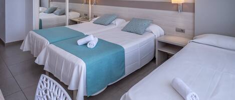 A hotel room with two beds, each with a white bedspread and a teal blanket. There are two bedside tables with lamps, a mirror, and a framed picture on the wall.