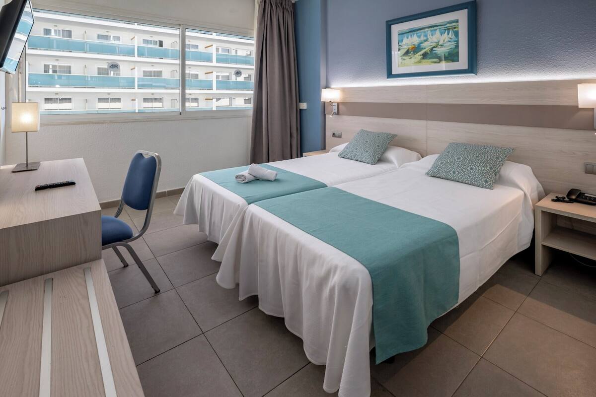 Quarto de hotel com duas camas, uma escrivaninha e uma cadeira.