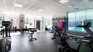 Une salle de sport équipée de divers appareils d’exercice, dotée d’une grande fenêtre et offrant une vue sur une piscine.