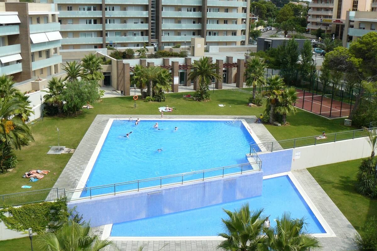 A swimming pool surrounded by palm trees and a building complex.