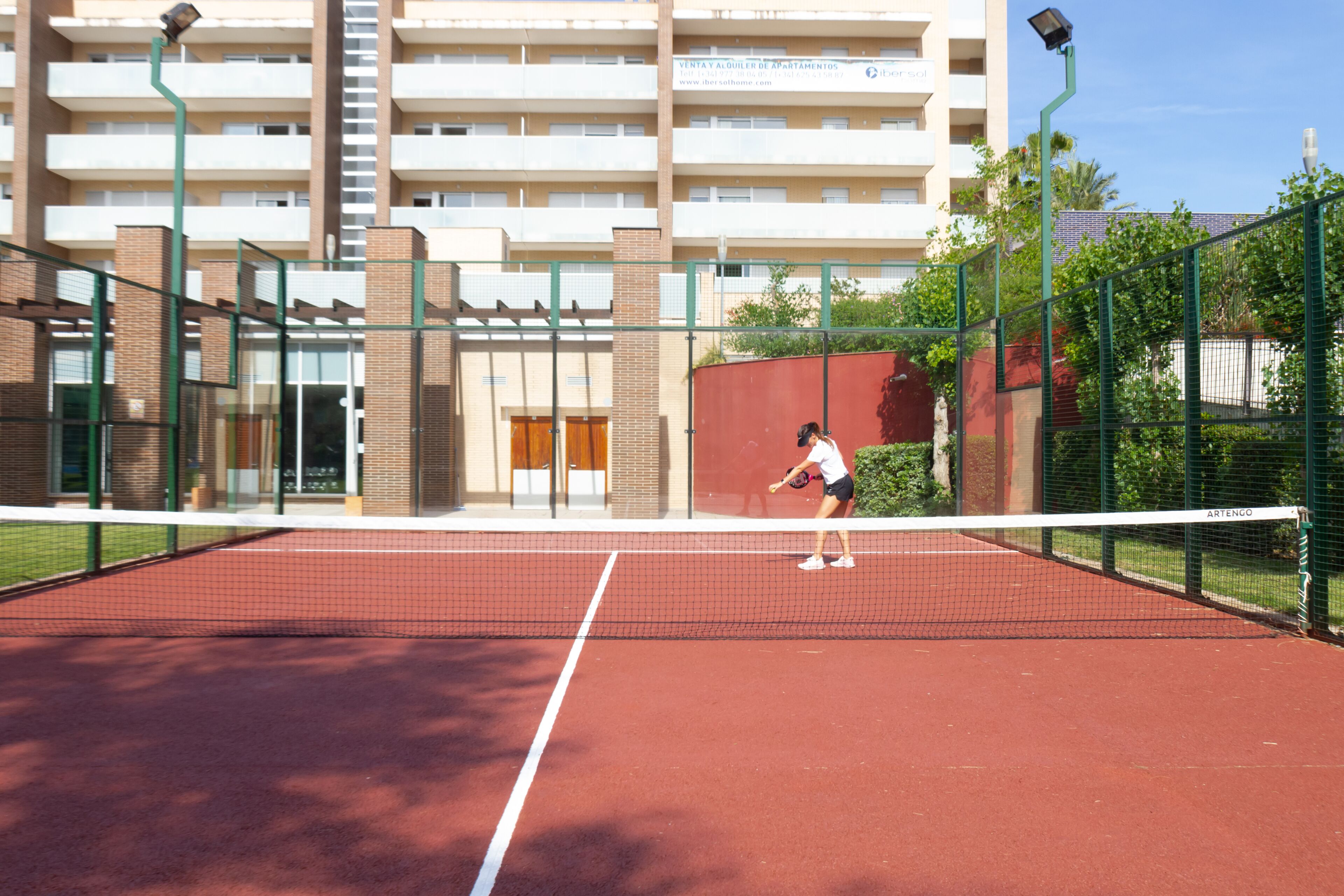 A tennis court with a net in the middle, surrounded by a fence.