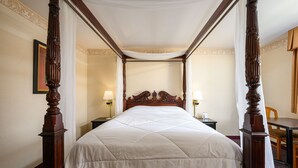 Una cama con dosel y cuatro columnas, dos mesitas de noche con lámparas y una silla en una habitación de hotel.