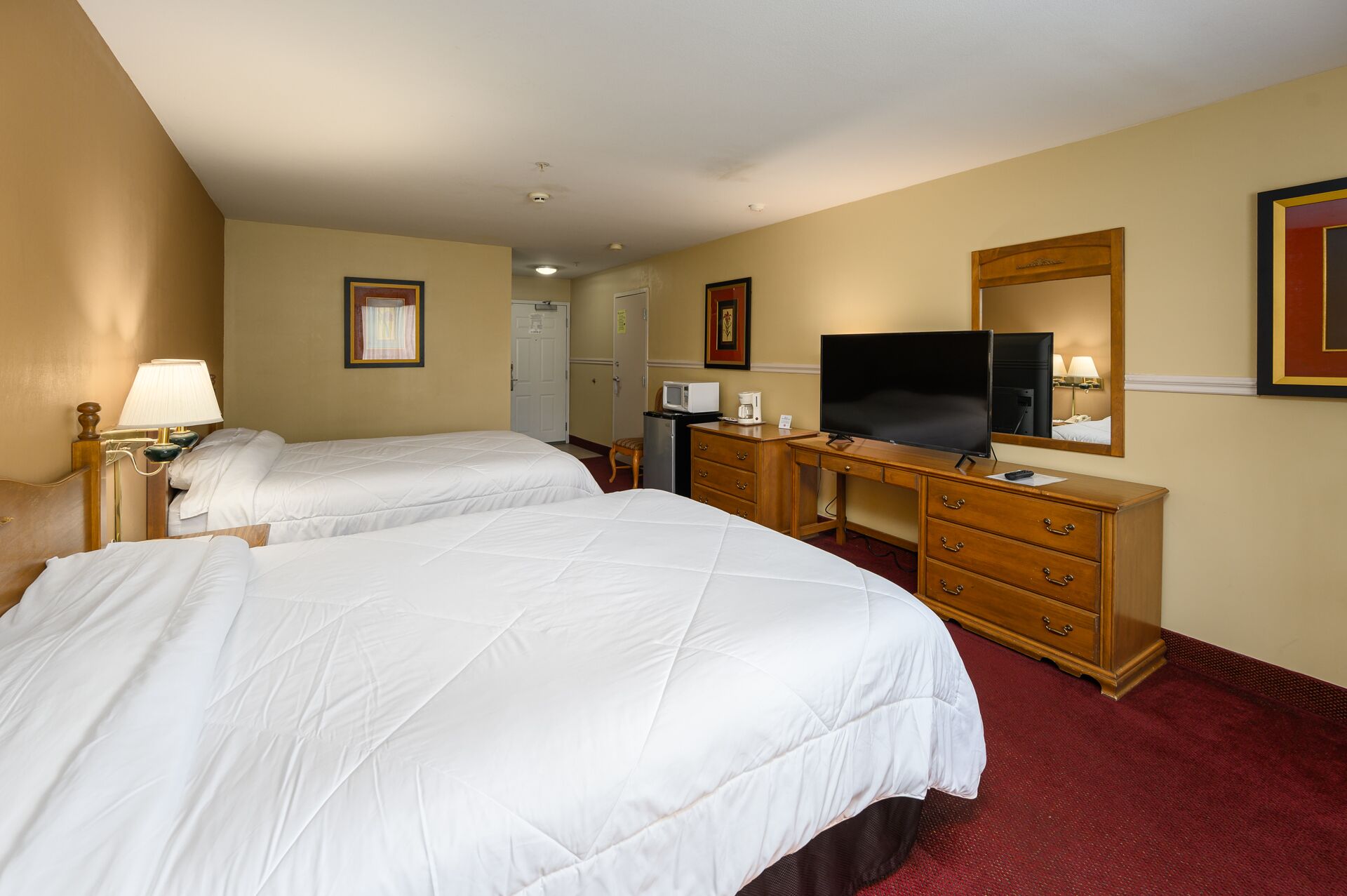 A hotel room with two beds, a desk with a television, a microwave, and a dresser.