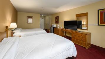 A hotel room with two beds, a desk with a television, a microwave, and a dresser.