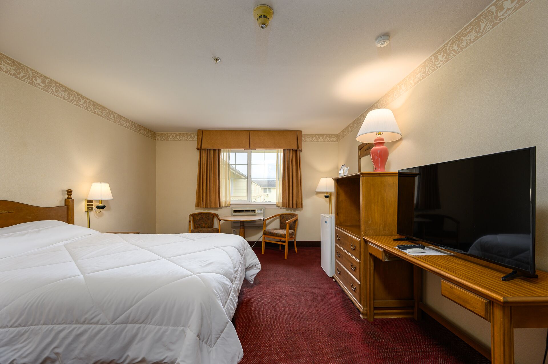A hotel room with two beds, a desk with a chair, a television, and a minibar.