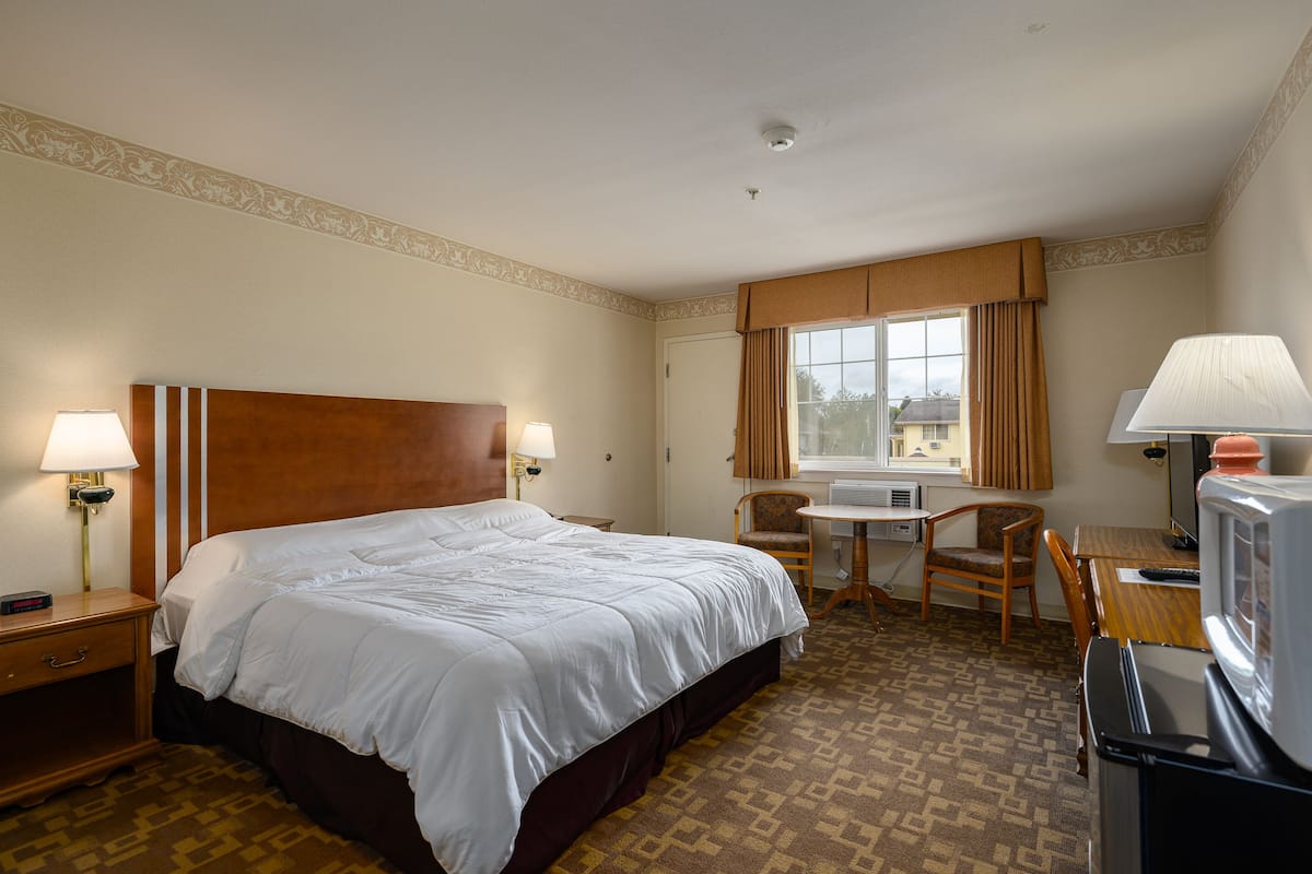 Una habitación de hotel con una cama grande, un escritorio con silla, televisión y una ventana con cortinas.