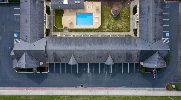 An aerial view of a hotel with a swimming pool, parking lot, and a gated entrance.