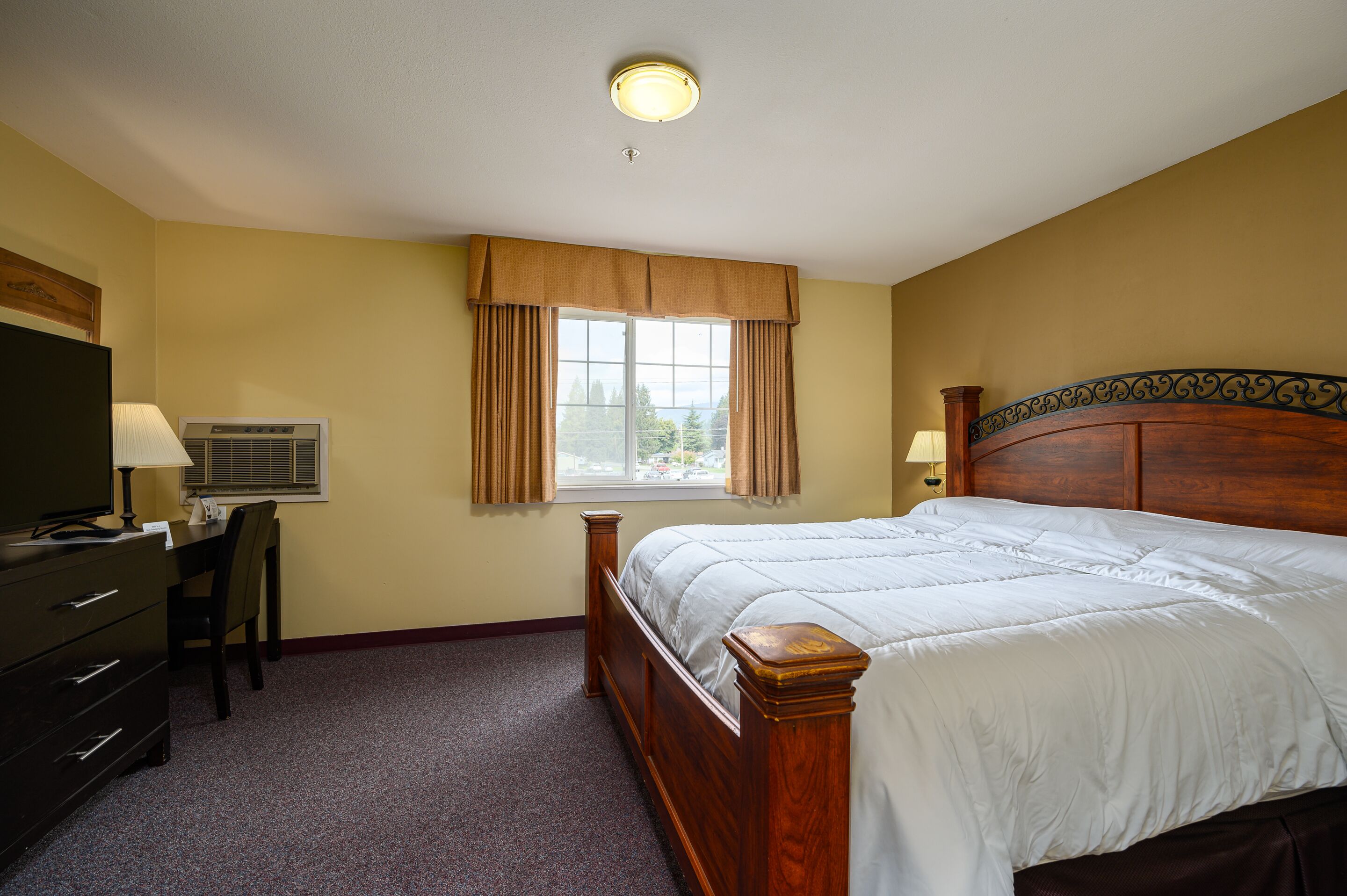 A bedroom with a bed, a desk, an air conditioning unit, and a window with curtains.