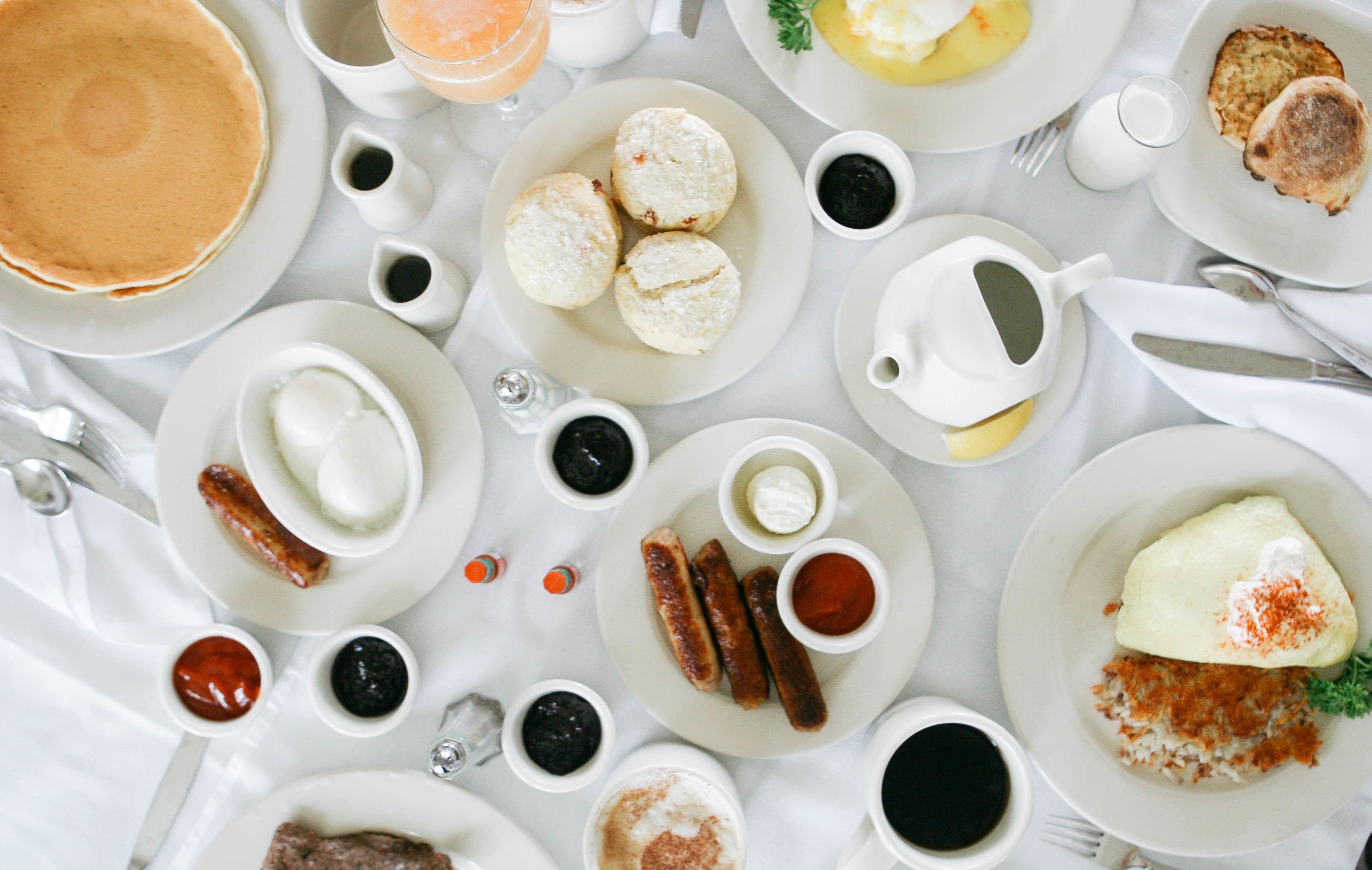 A breakfast table with various dishes including pancakes, sausages, eggs, and pastries.
