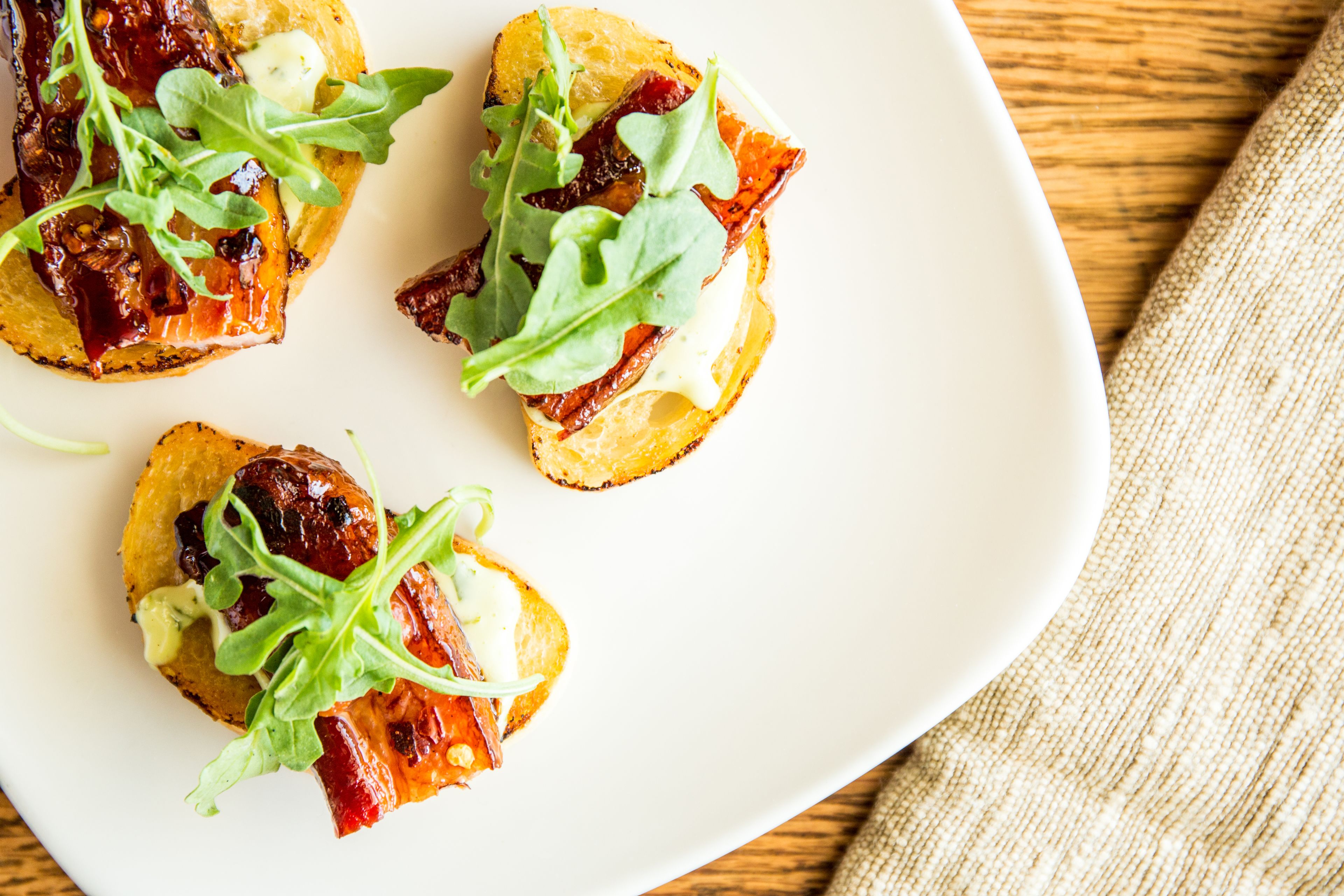 A white plate with four pieces of toast topped with greens and a creamy spread.