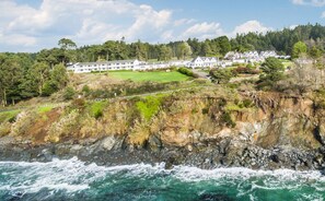 A coastal hotel with multiple buildings, a rocky shoreline, and a forested hill in the background. - Little River Inn (Little River)