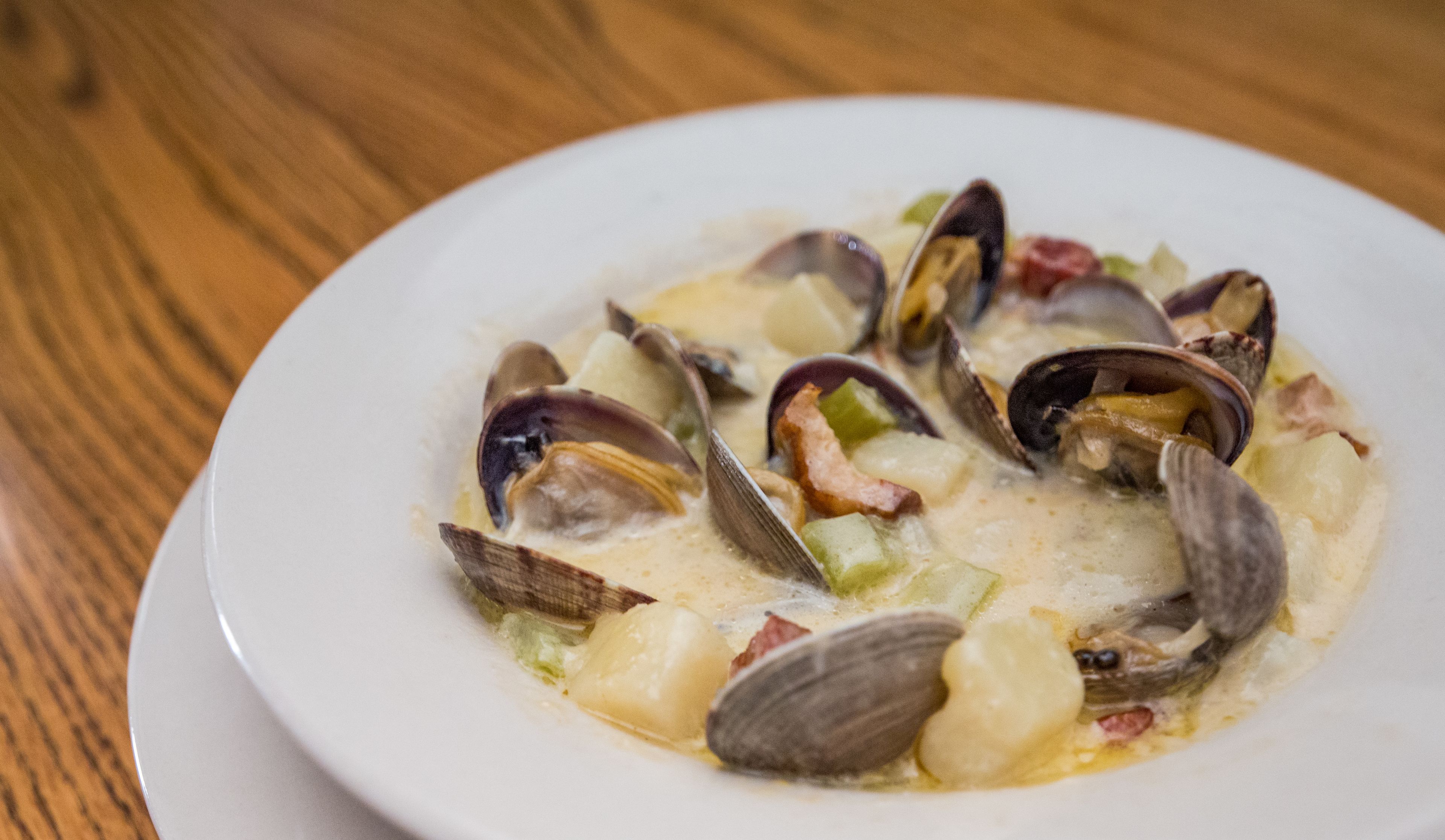 Un plato blanco con un guiso de mariscos, incluyendo almejas y patatas, sobre una mesa de madera.