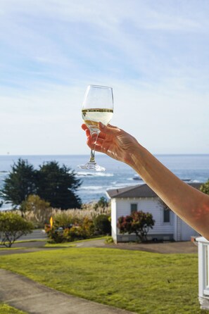 A hand holding a wine glass with a view of the ocean and a house in the background.