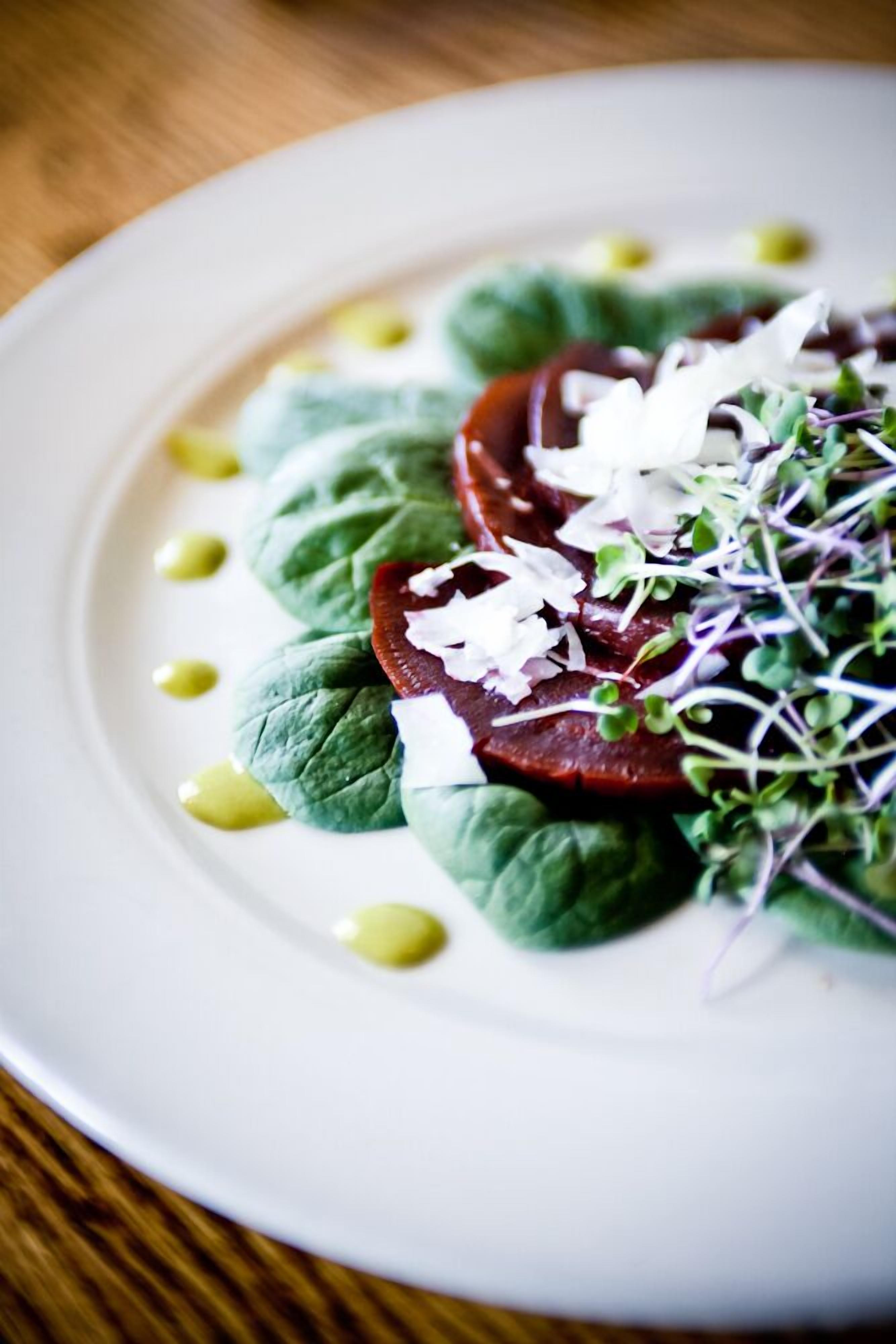 A white plate with a salad consisting of leafy greens, a slice of tomato, and sprouts, with a few green dots around.