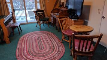 Un salon chaleureux avec une moquette verte, une table basse ronde en bois et un téléviseur posé sur un meuble en bois.