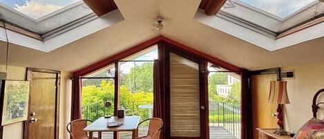 A bedroom with a skylight, a bed, a table with chairs, and a view of greenery outside.