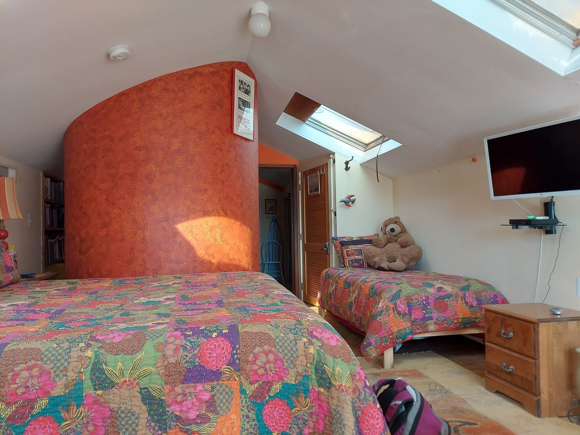 A bedroom with two beds, a large teddy bear, a TV, and a wooden nightstand.