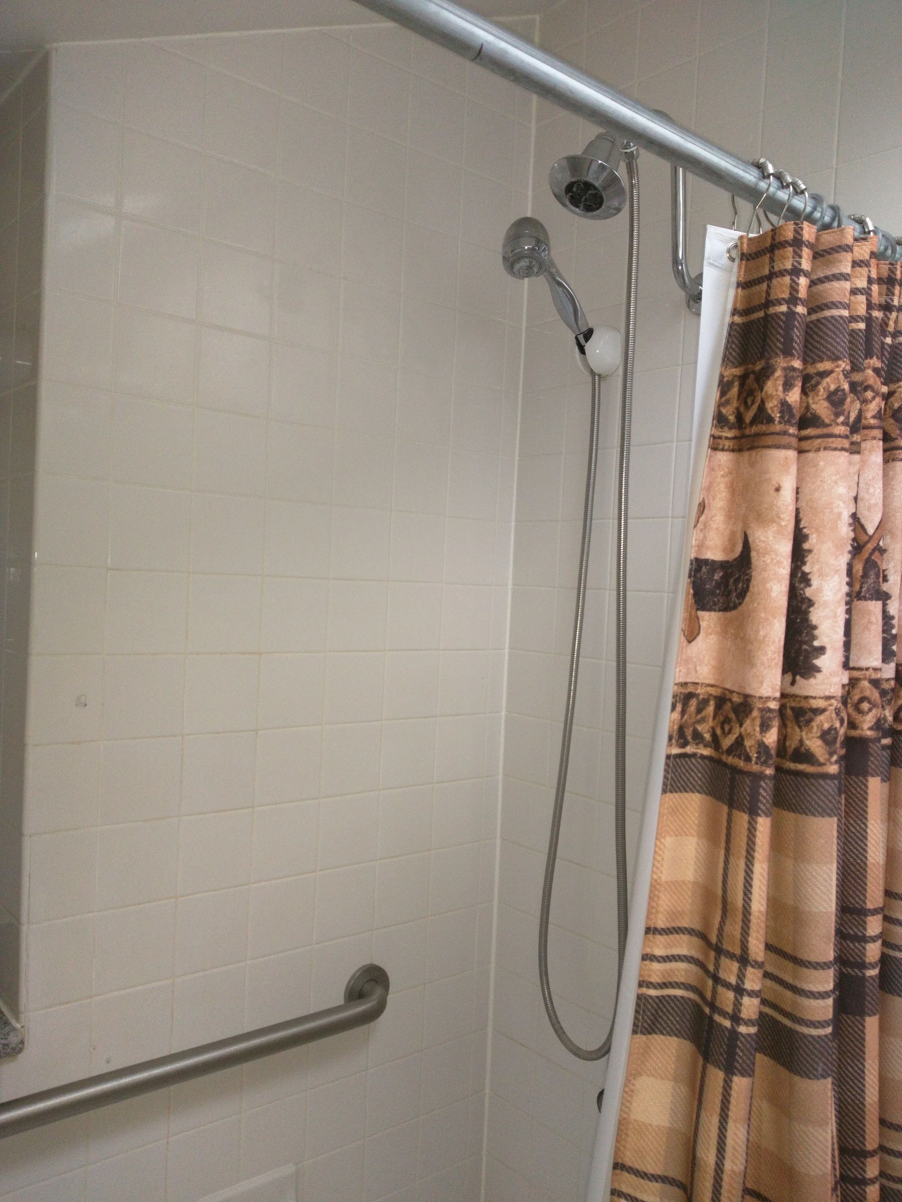 A shower with a metal grab bar, a showerhead, and a patterned shower curtain.