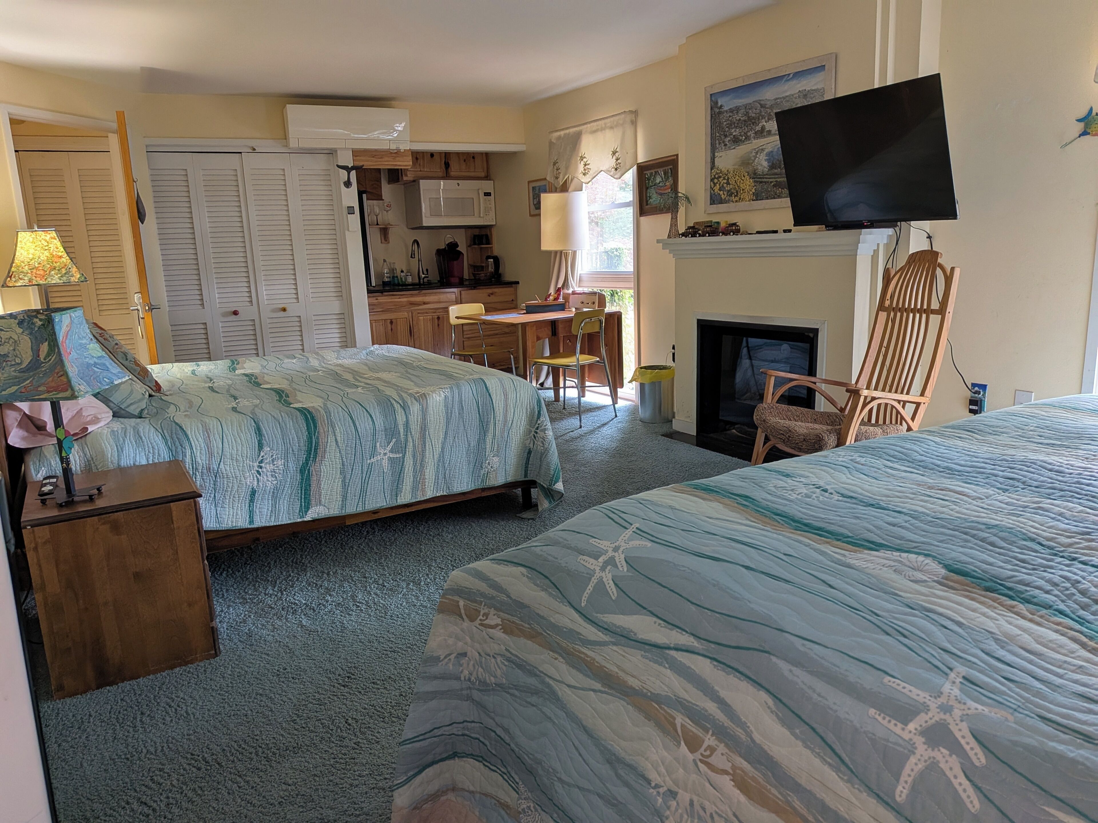 A hotel room with two beds, a TV, a fireplace, a kitchen area, and a dining table.