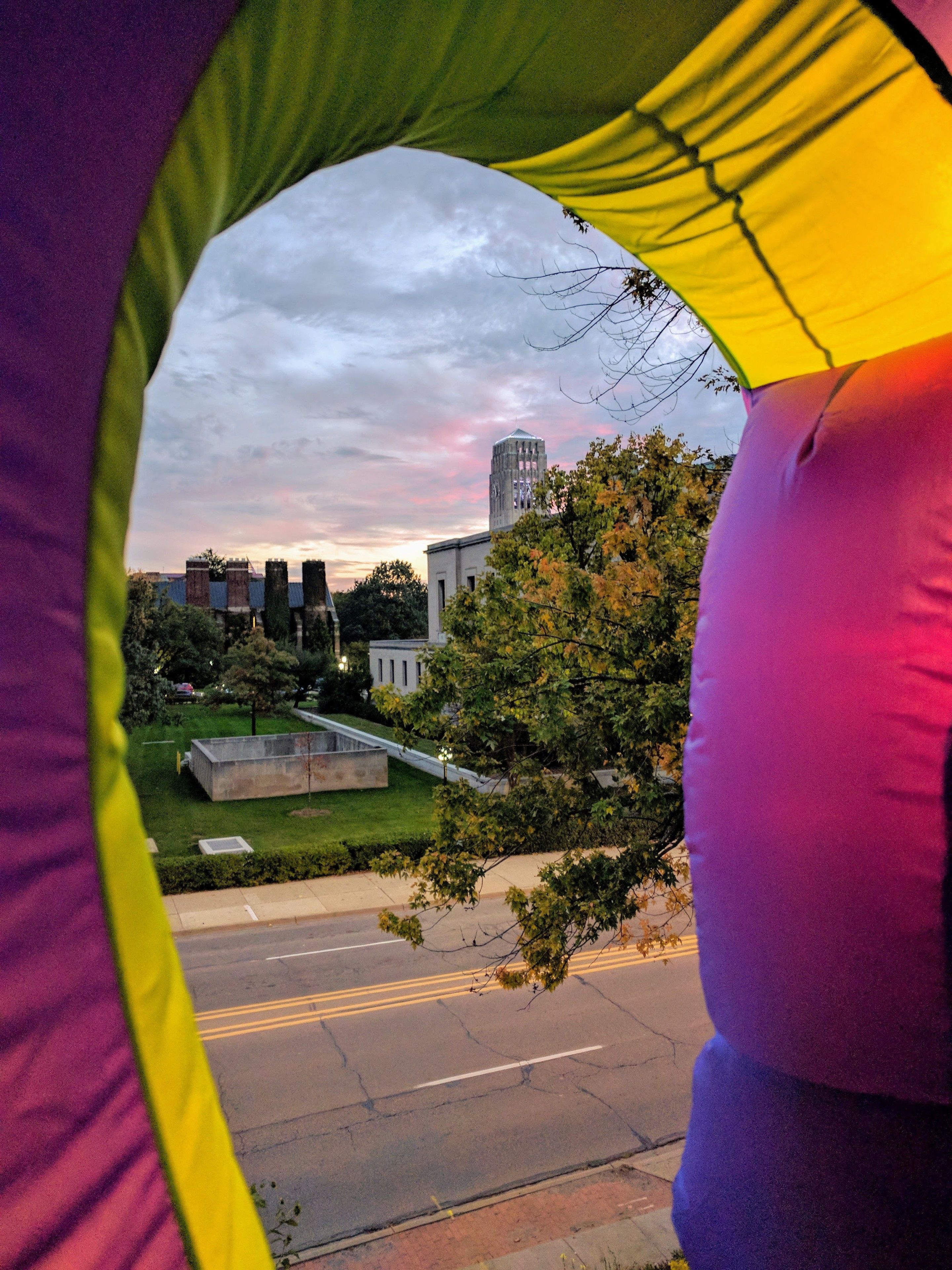 A view through a colorful window, revealing a cityscape with buildings, a road, and greenery.
