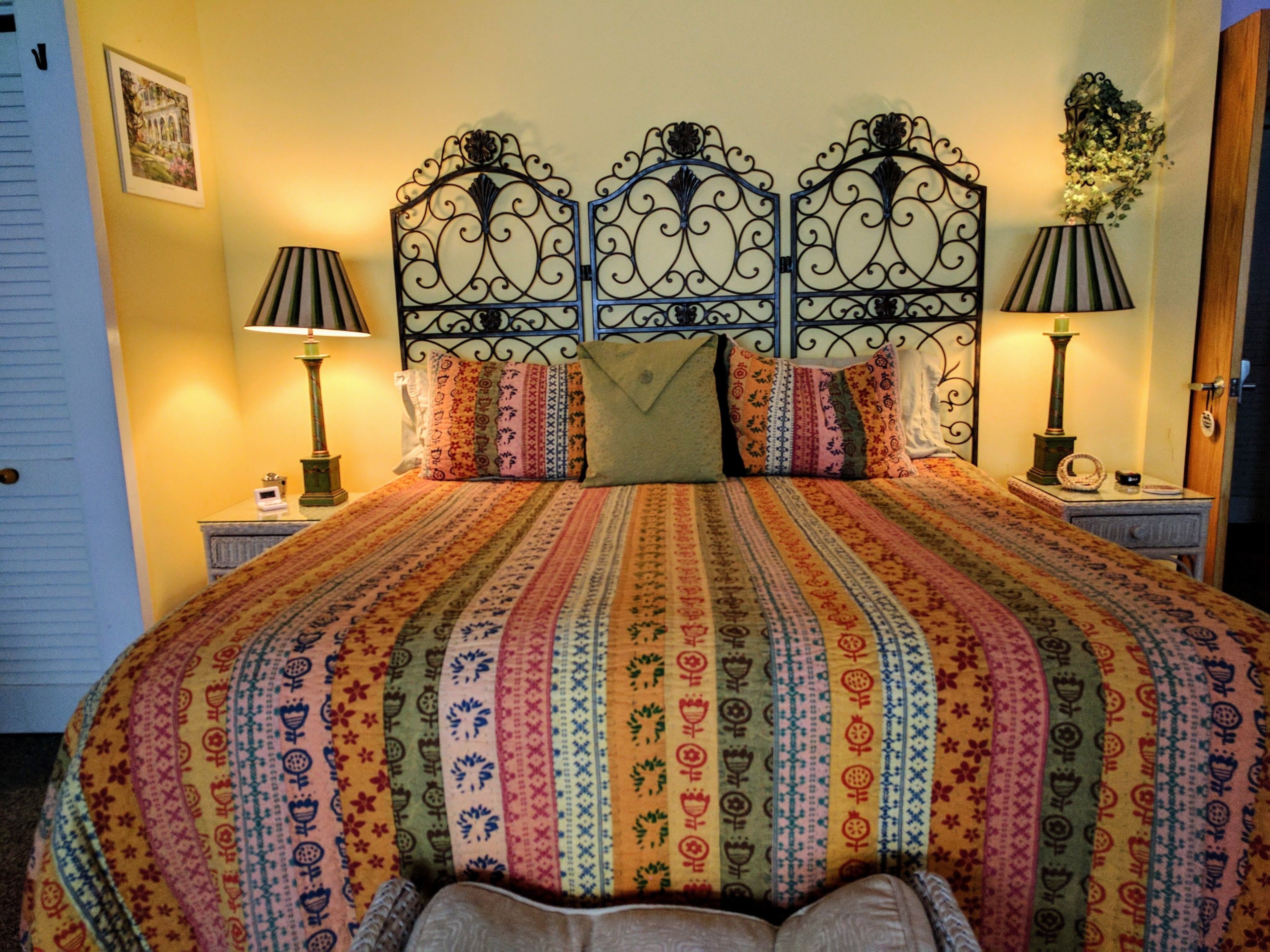 A bed with a patterned bedspread, two bedside lamps, and a decorative wall piece.